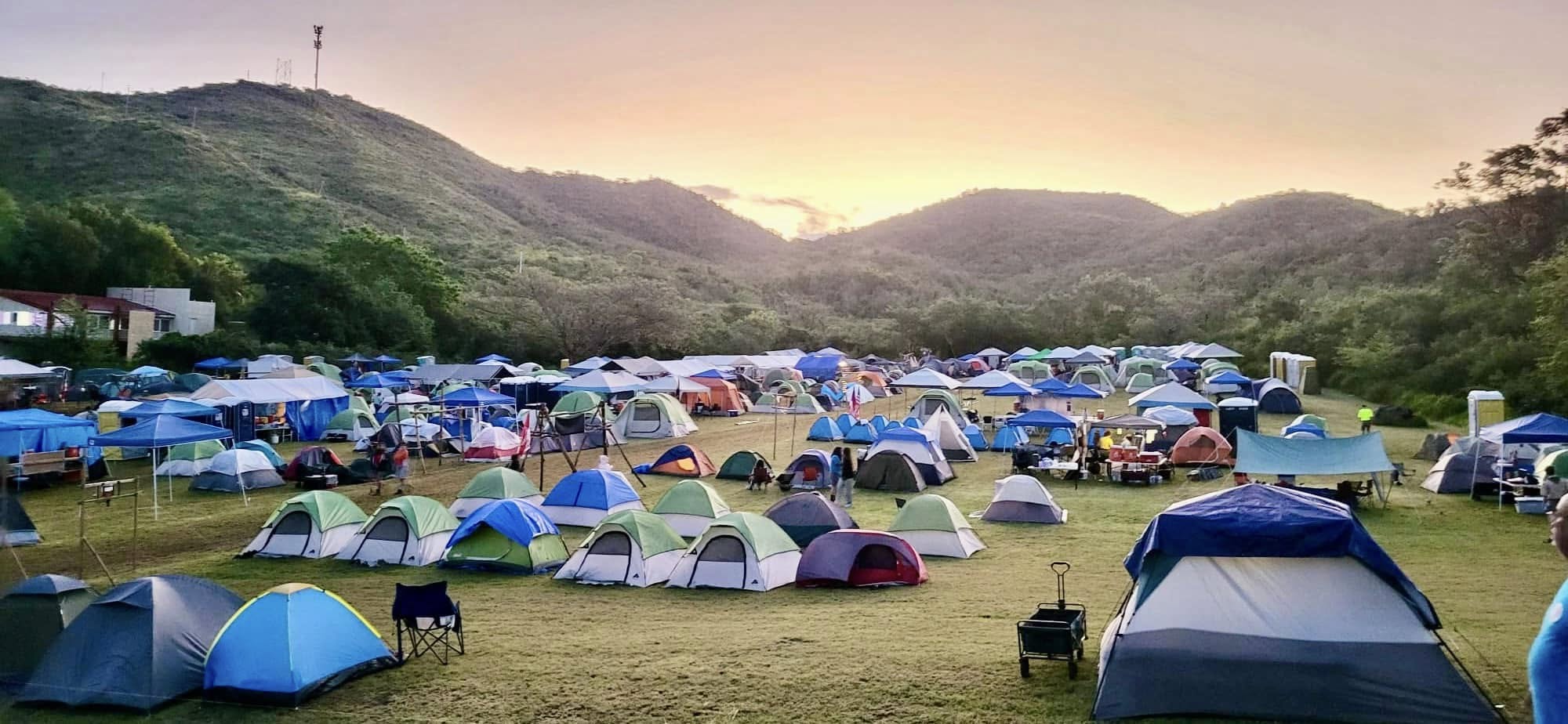 dozens of camping tents in a field surrounded by green hills